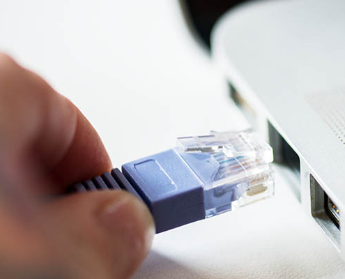 Hand plugging Ethernet network cable into laptop RJ45 port for internet connection