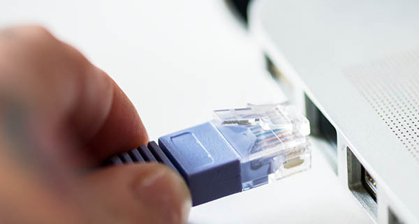 Hand plugging Ethernet network cable into laptop RJ45 port for internet connection