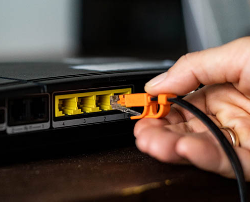 Router with four yellow RJ45 Ethernet LAN ports and a hand plugging in a network cable