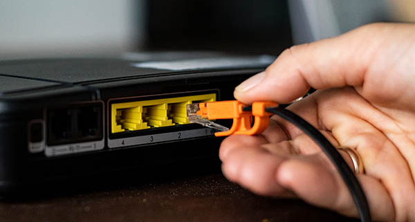 Router with four yellow RJ45 Ethernet LAN ports and a hand plugging in a network cable