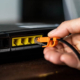 Router with four yellow RJ45 Ethernet LAN ports and a hand plugging in a network cable